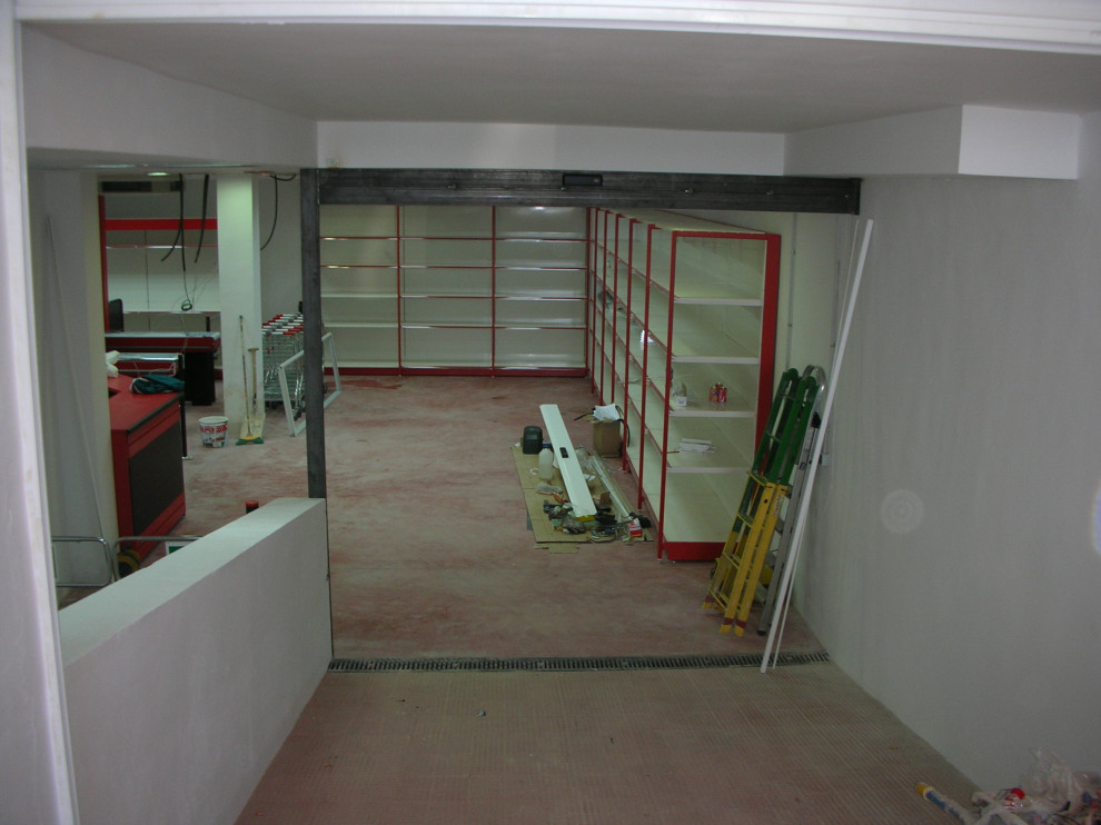 Photo of an expansive contemporary look-out basement in Other with white walls, concrete flooring and red floors.