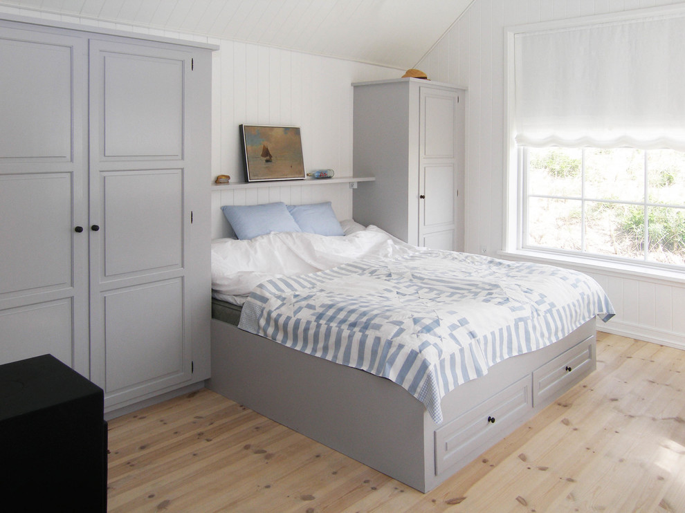 Diseño de dormitorio principal costero de tamaño medio sin chimenea con paredes blancas, suelo de madera clara y suelo beige
