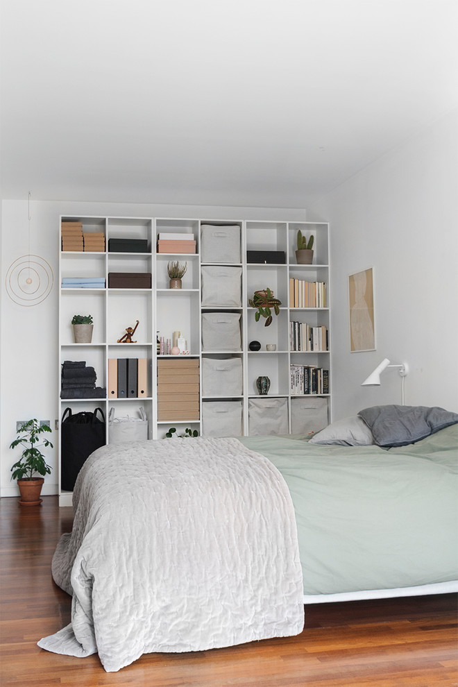 Modelo de dormitorio escandinavo con paredes blancas, suelo de madera en tonos medios y suelo marrón