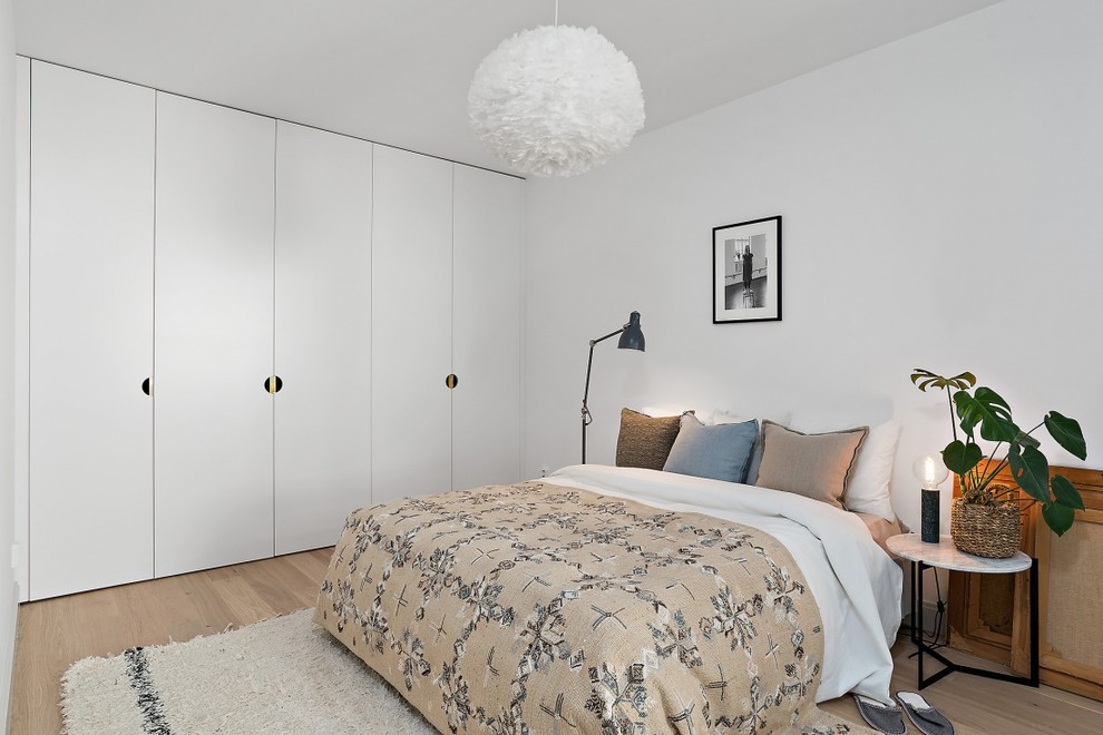 Ejemplo de dormitorio principal nórdico grande sin chimenea con suelo de madera clara y paredes blancas