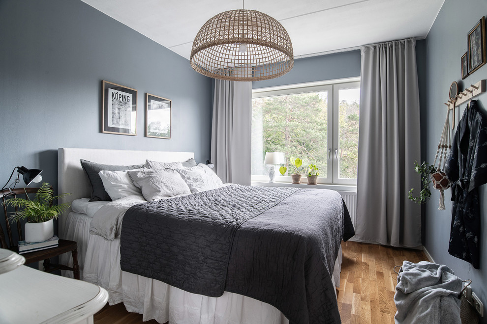 Bild på ett skandinaviskt sovrum, med blå väggar, mellanmörkt trägolv och brunt golv
