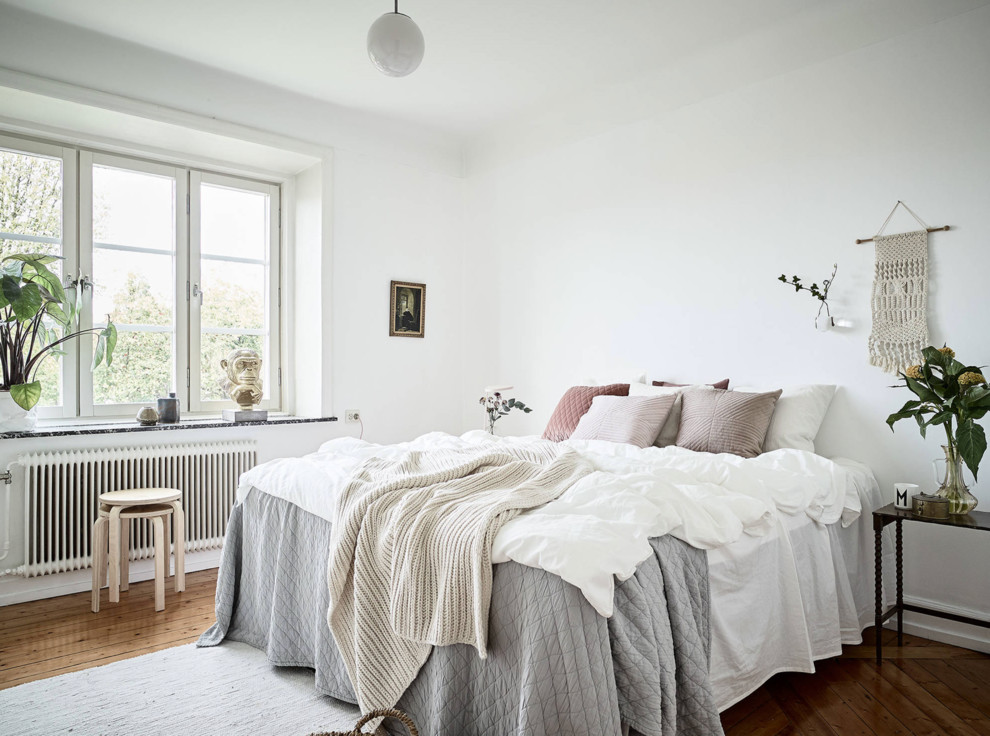 Ejemplo de dormitorio principal nórdico de tamaño medio sin chimenea con paredes blancas, suelo de madera en tonos medios y suelo marrón