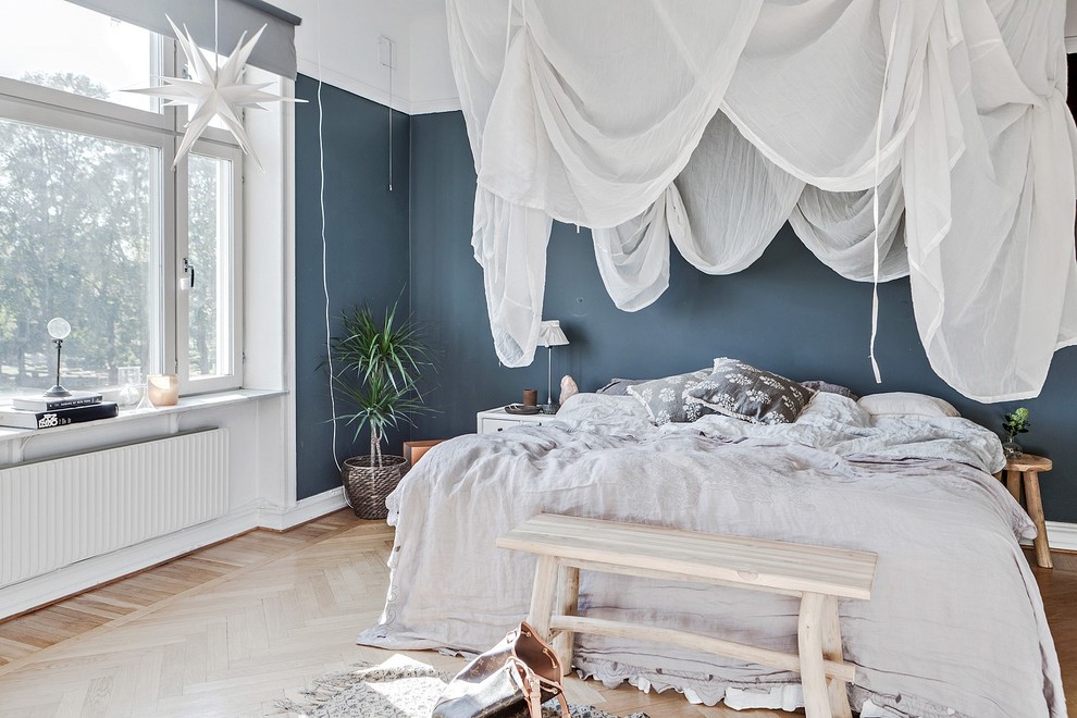 Inredning av ett minimalistiskt sovrum, med blå väggar, ljust trägolv och beiget golv