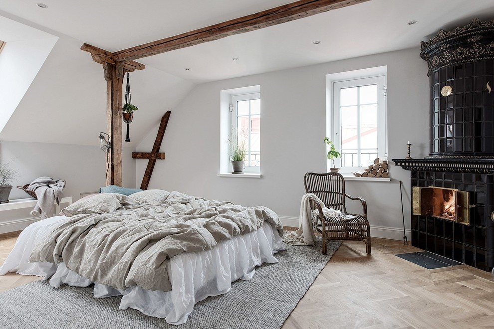 Imagen de dormitorio principal nórdico grande con paredes blancas, estufa de leña, marco de chimenea de baldosas y/o azulejos, suelo beige, suelo de madera clara y techo inclinado