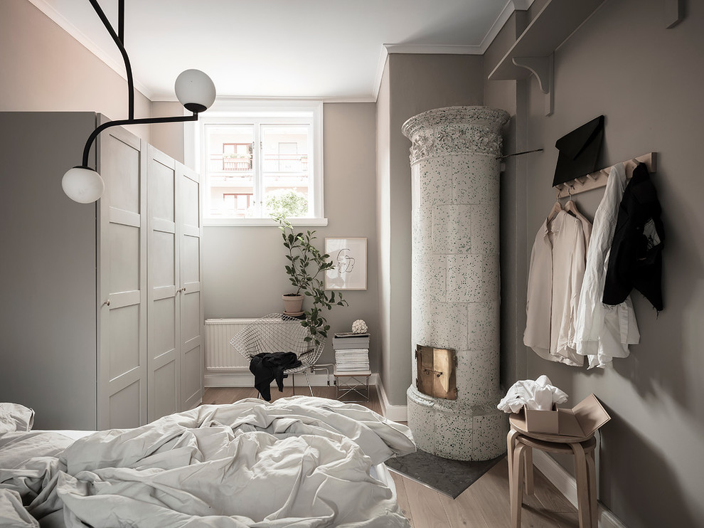 Idée de décoration pour une petite chambre nordique avec un mur gris, parquet clair, un sol beige, une cheminée d'angle et un manteau de cheminée en carrelage.