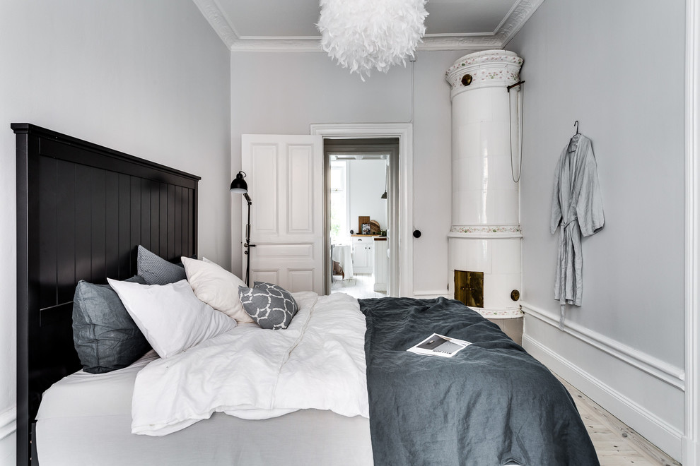 Esempio di una camera matrimoniale scandinava di medie dimensioni con camino ad angolo, pareti bianche e parquet chiaro