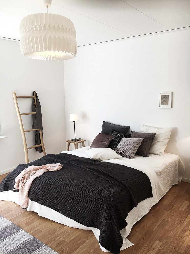 Imagen de dormitorio nórdico con paredes blancas, suelo de madera en tonos medios y suelo marrón