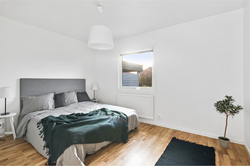 Diseño de habitación de invitados escandinava con paredes blancas, suelo de madera en tonos medios y suelo marrón