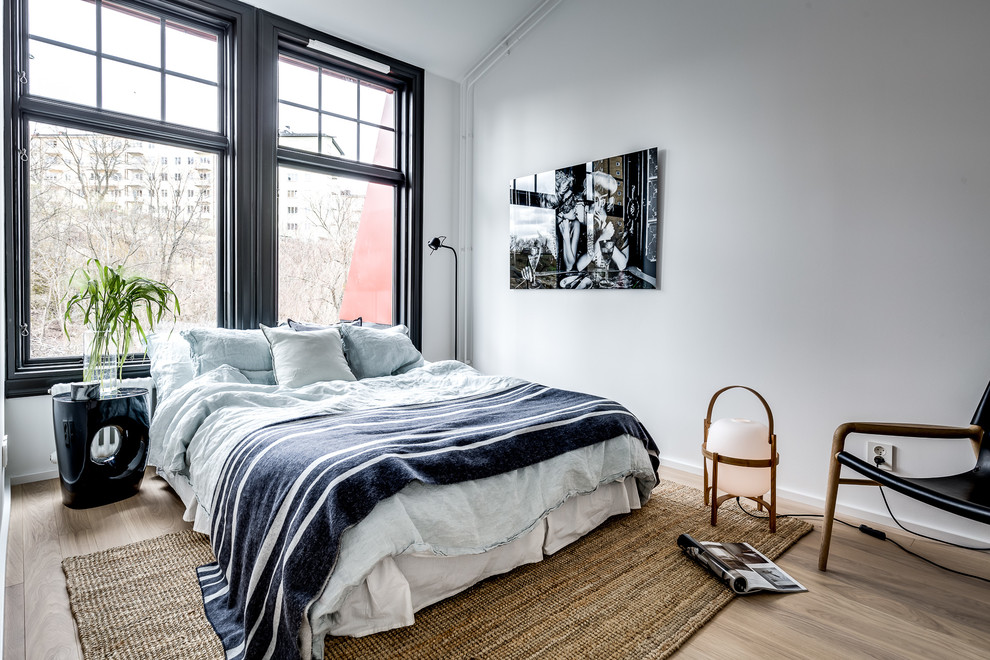 Scandinavian bedroom in Stockholm with white walls, light hardwood flooring and brown floors.