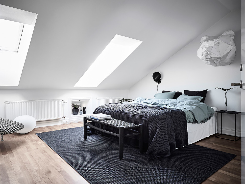 Bild på ett nordiskt sovrum, med vita väggar, mellanmörkt trägolv och brunt golv