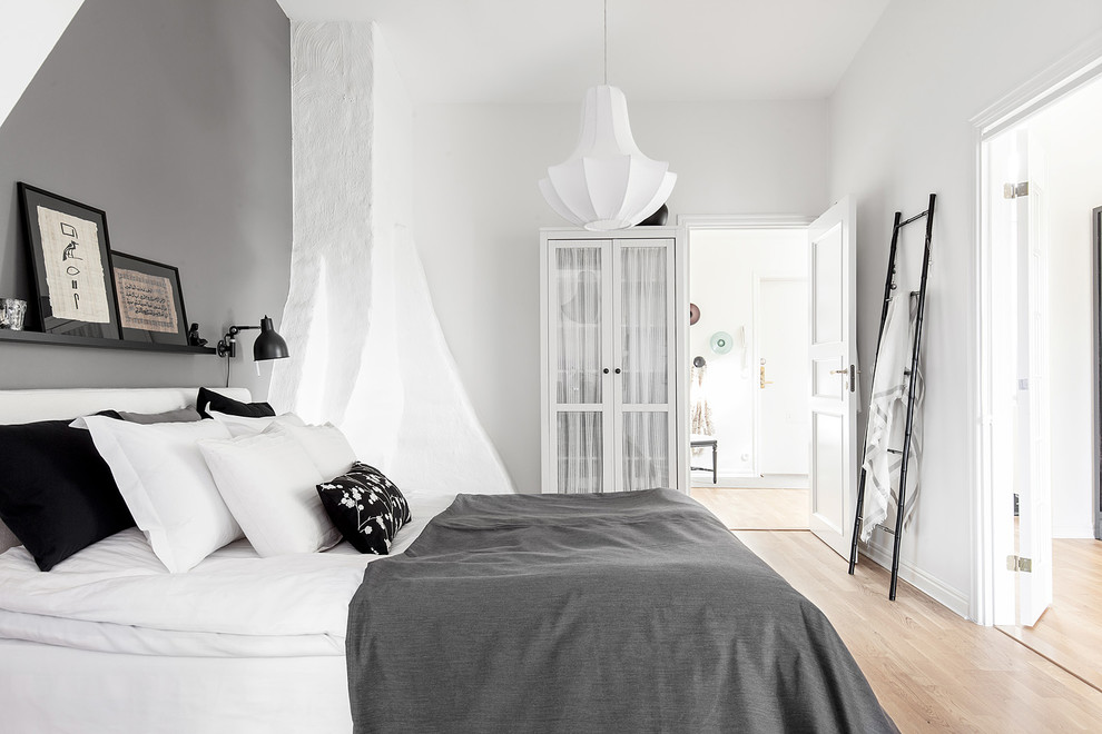 Modelo de dormitorio principal nórdico grande con paredes blancas, suelo de madera clara y suelo marrón