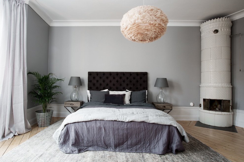 Ejemplo de dormitorio principal escandinavo de tamaño medio con paredes grises, suelo de madera clara, estufa de leña y marco de chimenea de baldosas y/o azulejos