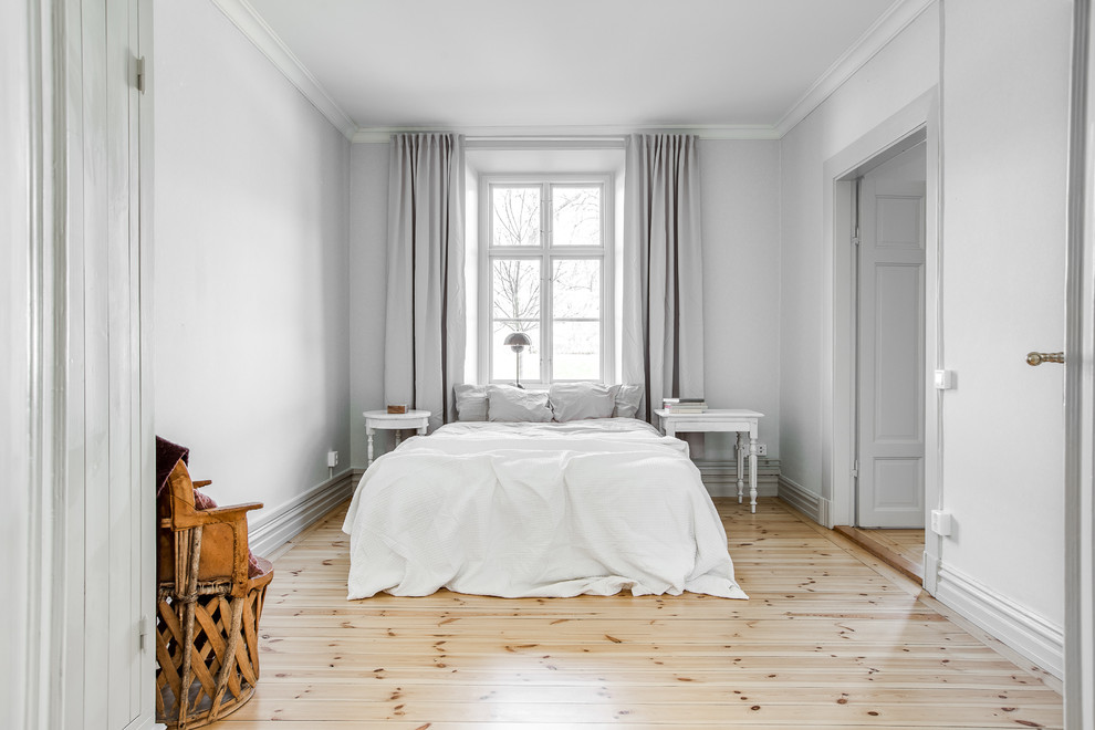 Ejemplo de dormitorio principal escandinavo sin chimenea con paredes blancas y suelo de madera clara