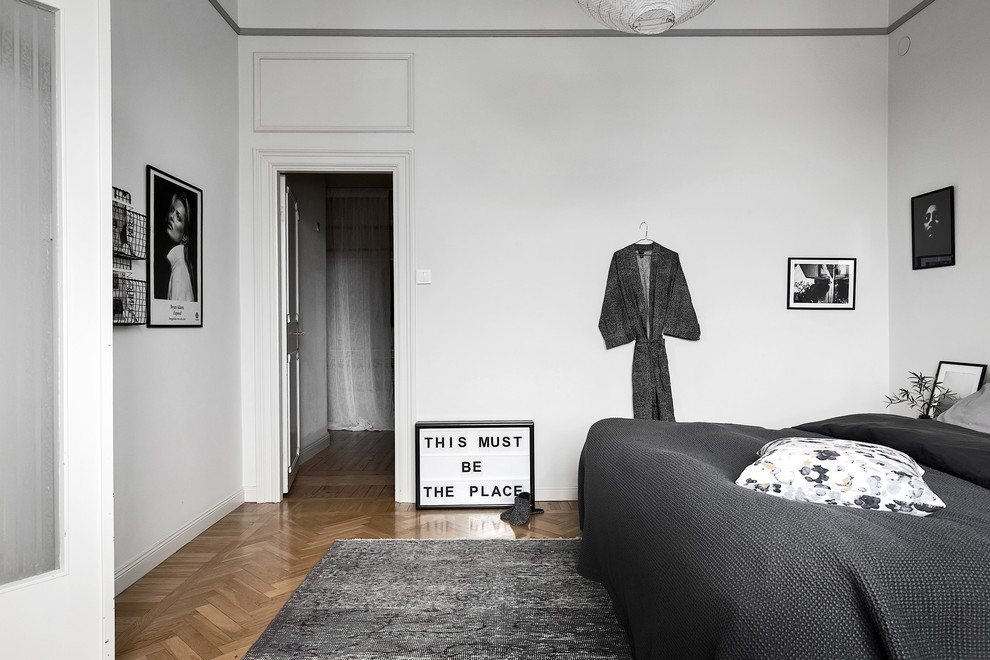 На фото: серо-белая спальня в скандинавском стиле с белыми стенами, паркетным полом среднего тона и бежевым полом с