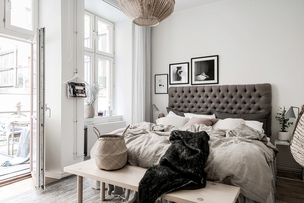 Bild på ett nordiskt sovrum, med vita väggar, mellanmörkt trägolv och brunt golv