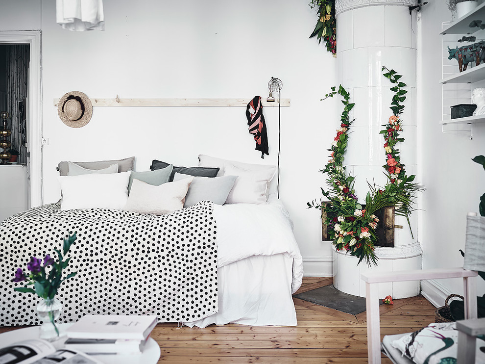 Imagen de dormitorio nórdico con paredes blancas, suelo de madera en tonos medios, suelo beige y chimenea de esquina