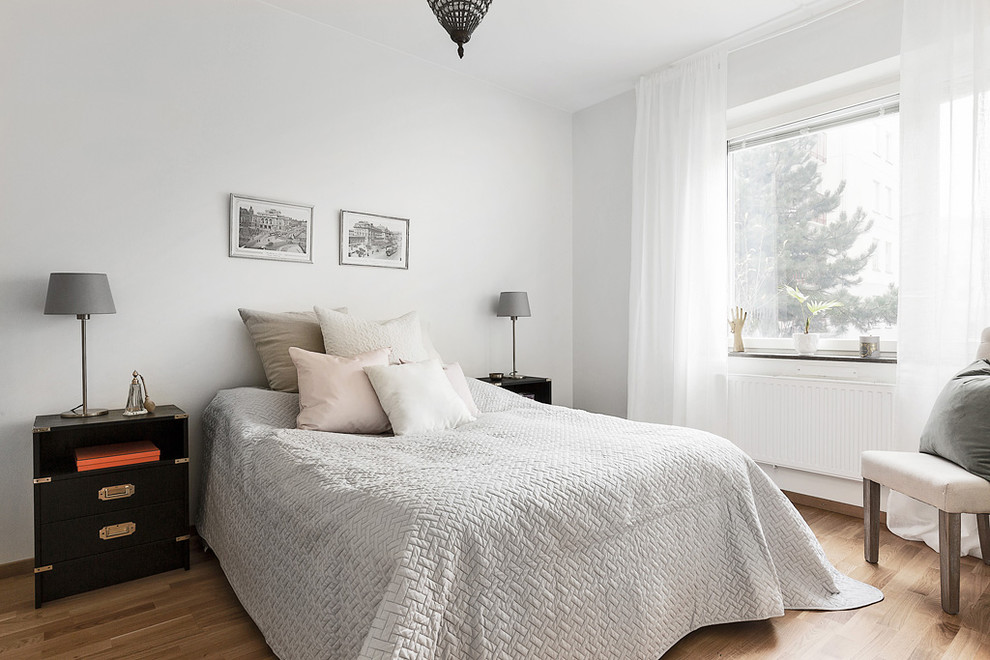 This is an example of a medium sized scandi master bedroom in Stockholm with white walls and light hardwood flooring.