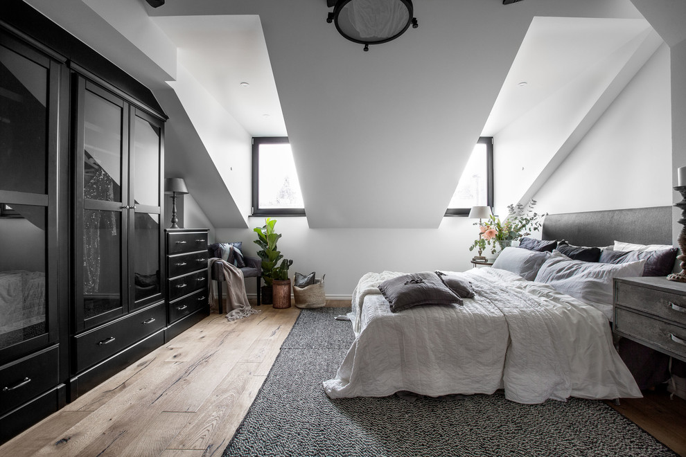 Photo of a large scandi master loft bedroom in Stockholm with white walls and light hardwood flooring.