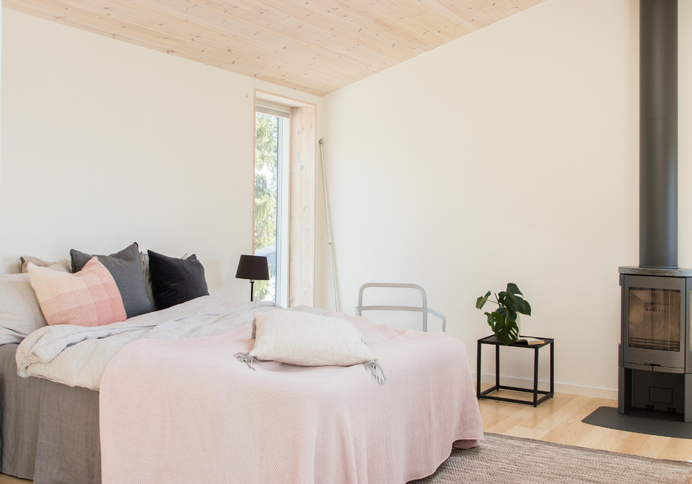 Idee per una camera matrimoniale nordica con pareti bianche, parquet chiaro, stufa a legna, cornice del camino in metallo e pavimento beige