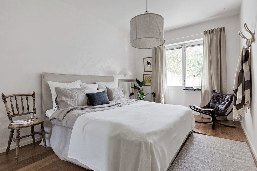 Idéer för att renovera ett minimalistiskt sovrum, med vita väggar, mellanmörkt trägolv och brunt golv