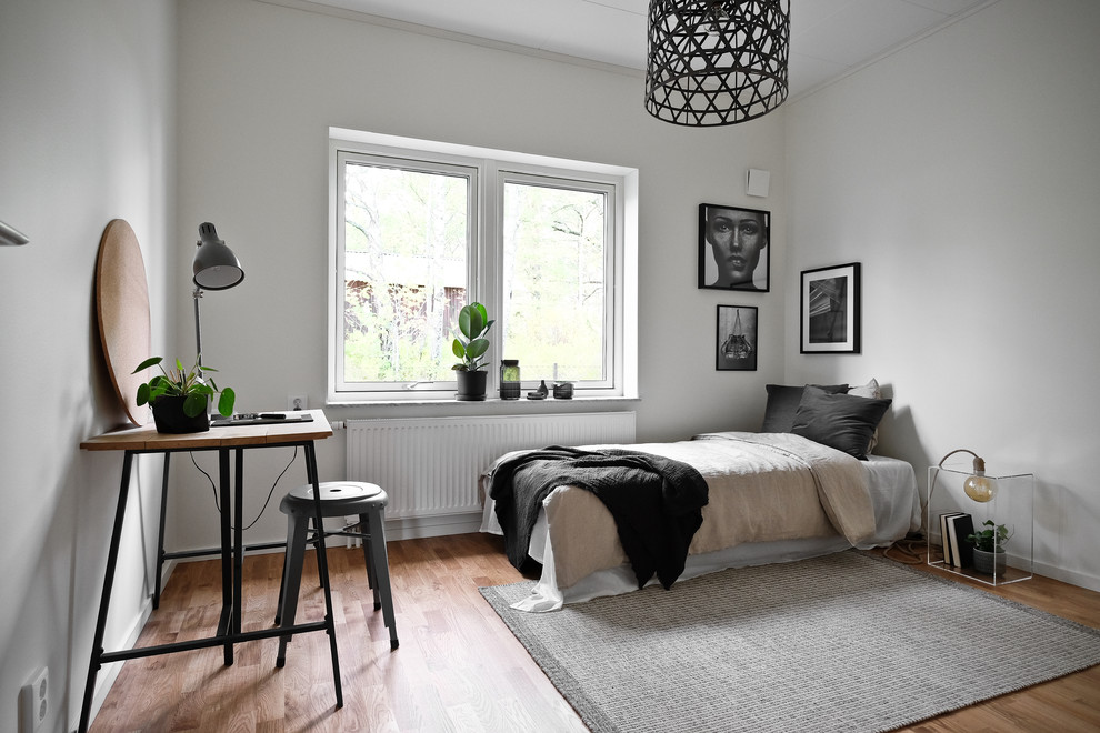 Nordisk inredning av ett mellanstort sovrum, med vita väggar, mellanmörkt trägolv och brunt golv