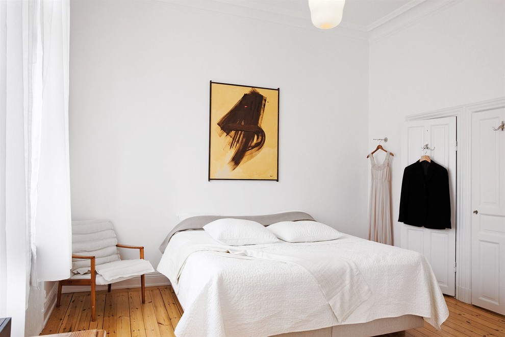 Large scandi master bedroom in Stockholm with white walls, medium hardwood flooring and no fireplace.