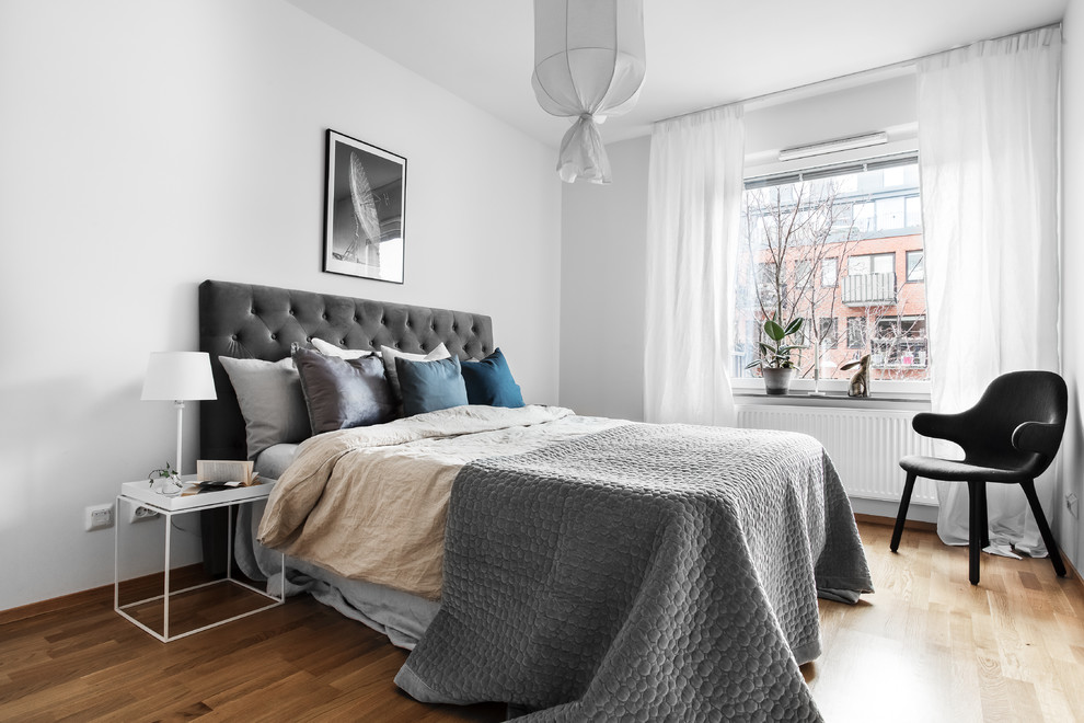 Scandinavian guest and grey and brown bedroom in Stockholm with grey walls, medium hardwood flooring and brown floors.
