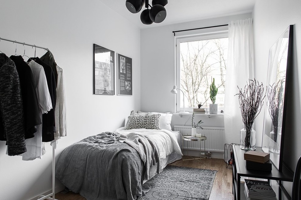 Ejemplo de habitación de invitados gris y blanca nórdica de tamaño medio sin chimenea con paredes blancas y suelo de madera en tonos medios
