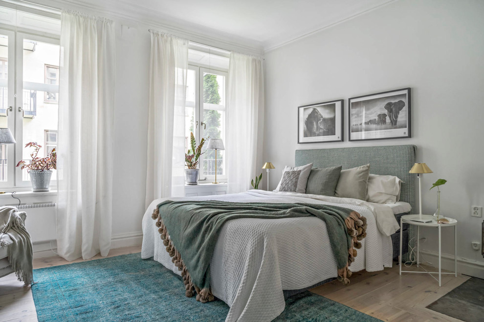 Bild på ett skandinaviskt sovrum, med vita väggar, ljust trägolv och beiget golv