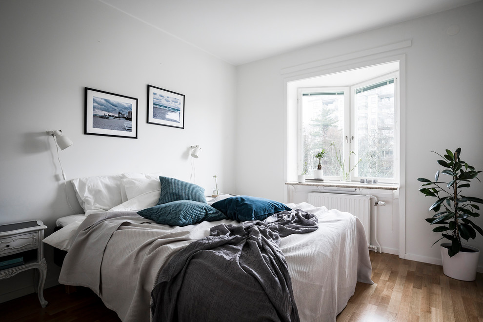Bild på ett skandinaviskt sovrum, med vita väggar och ljust trägolv