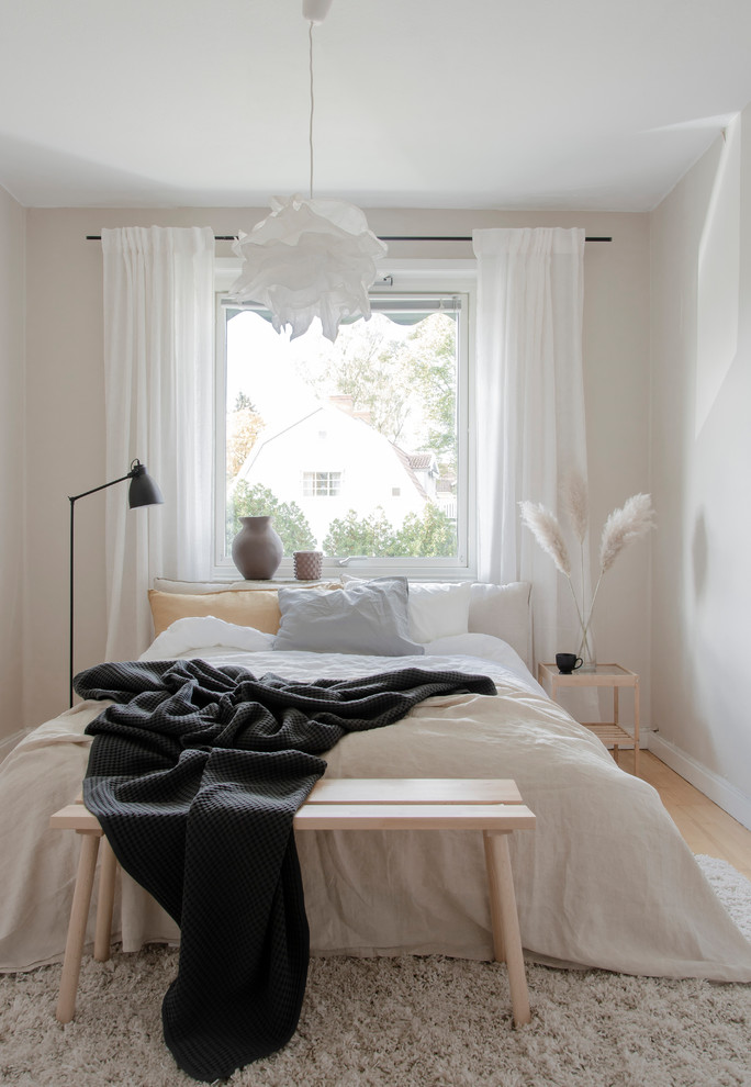 Skandinavisches Schlafzimmer mit beiger Wandfarbe, hellem Holzboden und beigem Boden in Örebro