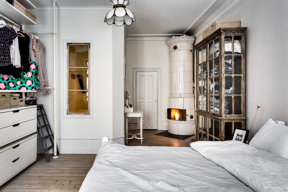 Mittelgroßes Klassisches Schlafzimmer mit weißer Wandfarbe, hellem Holzboden und Eckkamin in Stockholm