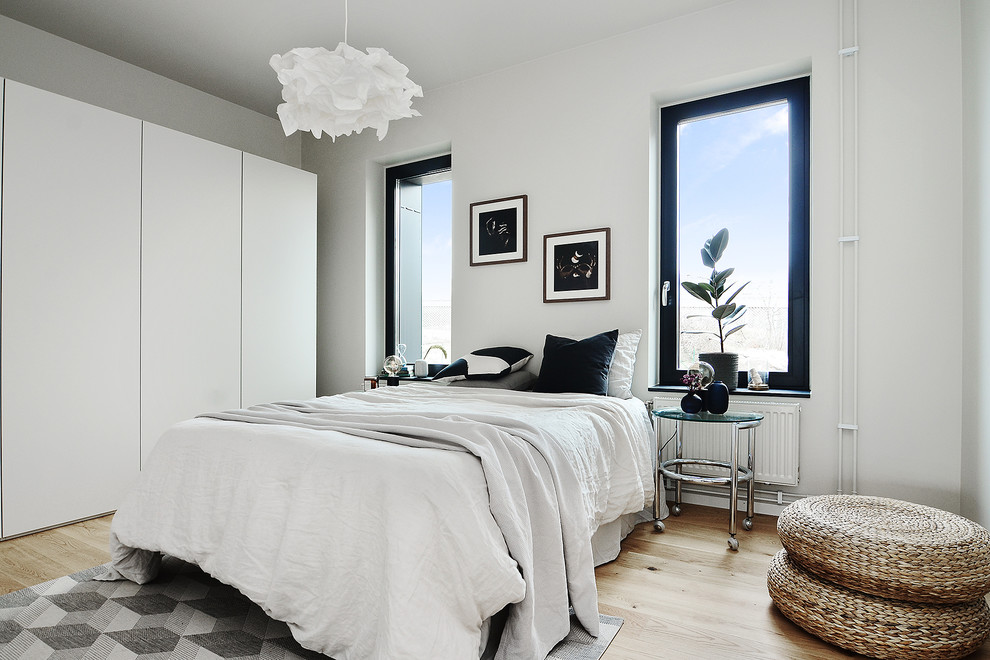 Scandi guest bedroom in Stockholm with white walls, light hardwood flooring and beige floors.