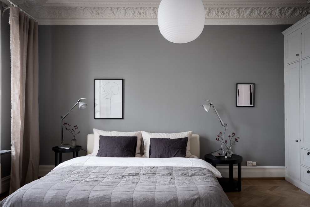 Inredning av ett minimalistiskt sovrum, med grå väggar, mellanmörkt trägolv och brunt golv