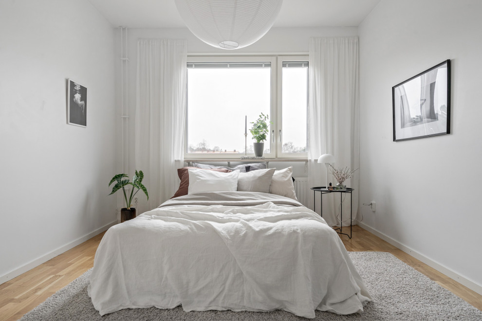 Medium sized scandi master bedroom in Stockholm with white walls, light hardwood flooring and beige floors.