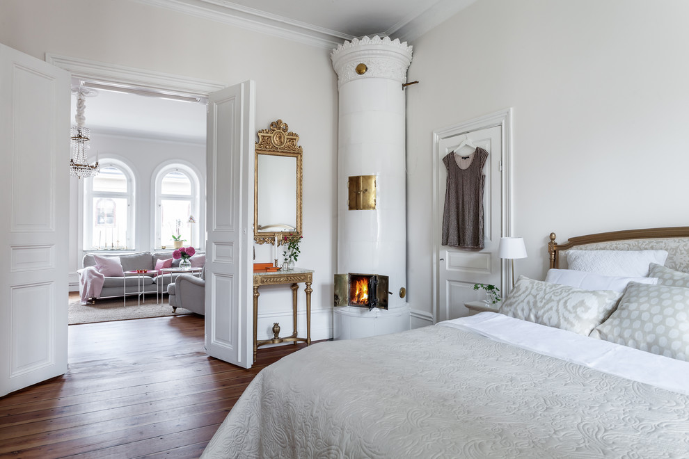 Großes Klassisches Hauptschlafzimmer mit weißer Wandfarbe, dunklem Holzboden und Kaminofen in Stockholm
