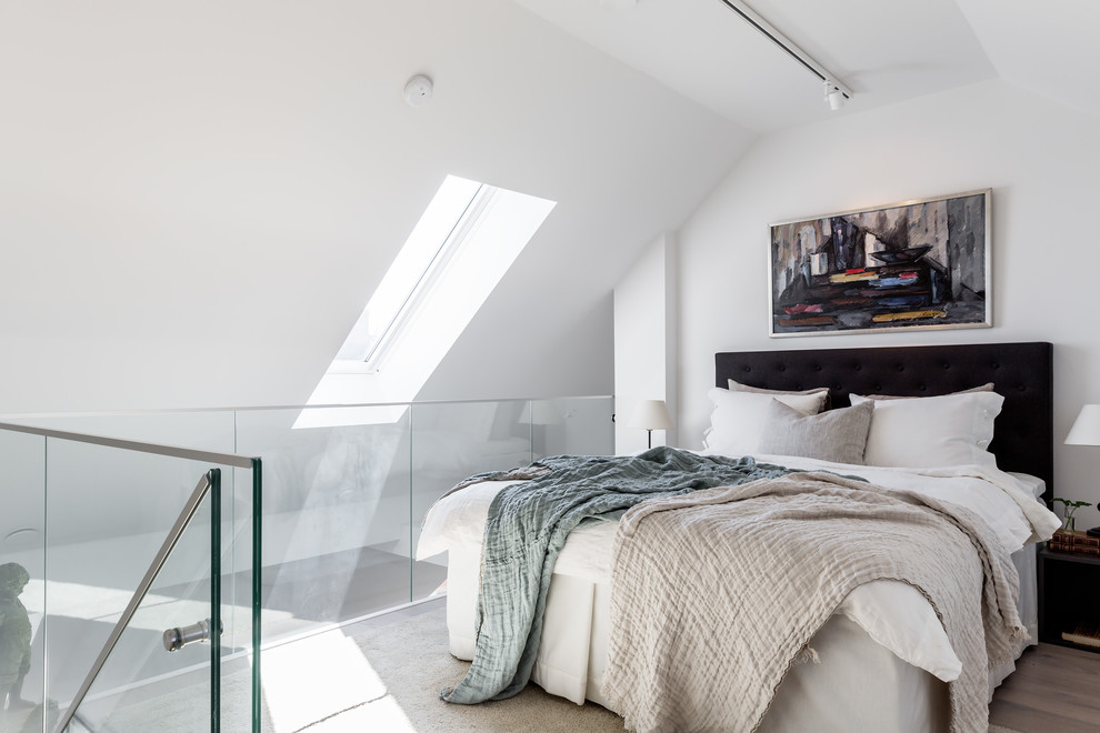 Modelo de dormitorio tipo loft escandinavo con paredes blancas, suelo de madera en tonos medios, suelo marrón y techo inclinado