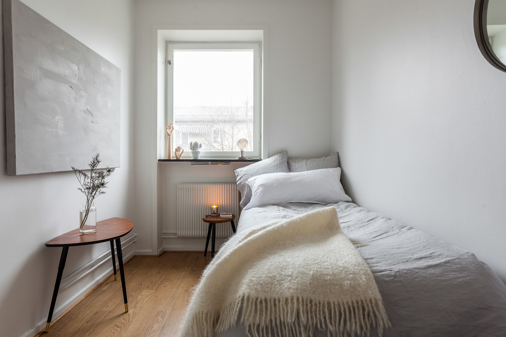 Modelo de habitación de invitados escandinava sin chimenea con paredes blancas y suelo de madera en tonos medios