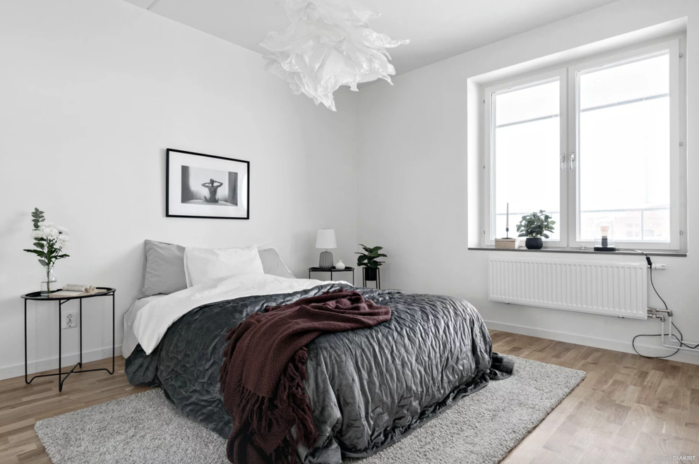 Medium sized modern master bedroom in Stockholm with white walls, light hardwood flooring and beige floors.