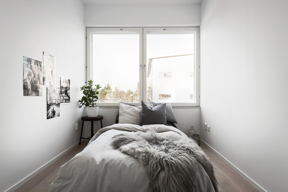 Mid-sized danish medium tone wood floor bedroom photo in Stockholm with white walls