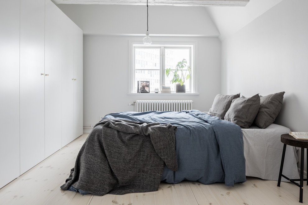 Inredning av ett minimalistiskt mellanstort sovrum, med vita väggar, ljust trägolv och beiget golv