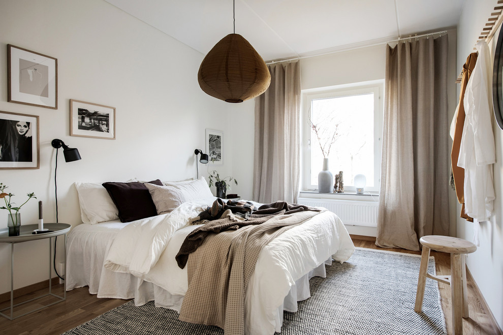 Пример оригинального дизайна: хозяйская спальня в скандинавском стиле с белыми стенами и паркетным полом среднего тона без камина