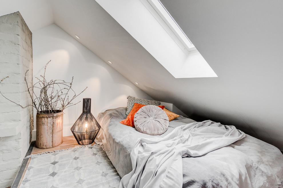 Diseño de habitación de invitados escandinava pequeña sin chimenea con paredes blancas, suelo de madera clara, suelo marrón y techo inclinado
