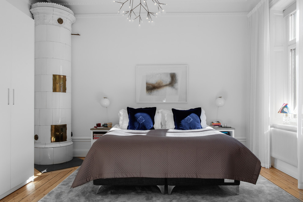 На фото: хозяйская спальня среднего размера в скандинавском стиле с белыми стенами, паркетным полом среднего тона, печью-буржуйкой, фасадом камина из плитки и бежевым полом