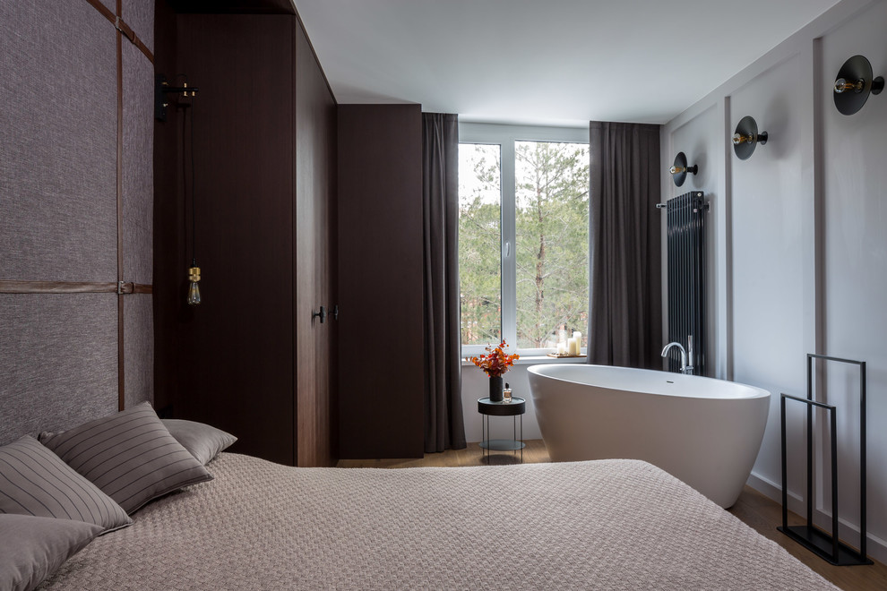 Diseño de dormitorio principal actual de tamaño medio sin chimenea con paredes blancas, suelo de madera en tonos medios y suelo marrón