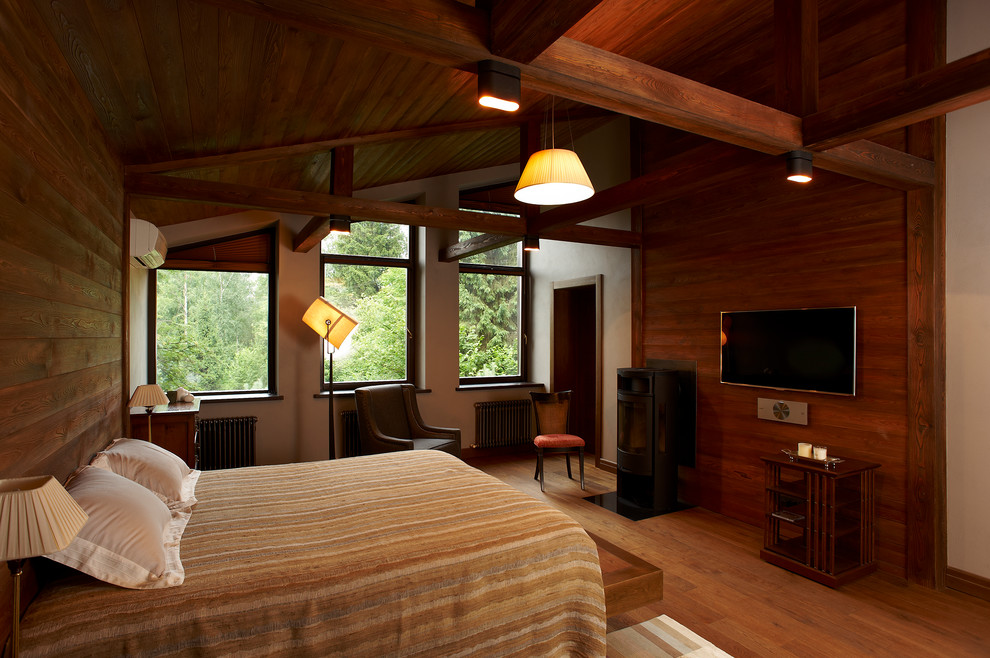 Foto de dormitorio principal actual de tamaño medio con paredes grises, suelo de madera pintada, estufa de leña, marco de chimenea de metal y suelo marrón