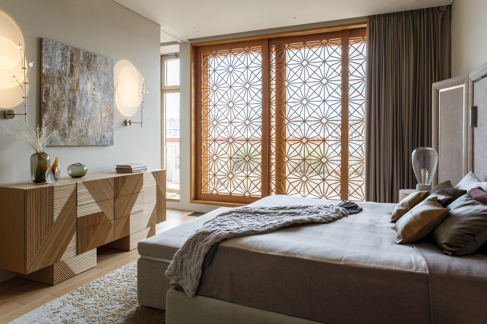 Modelo de dormitorio principal actual con paredes beige, suelo de madera clara y suelo beige