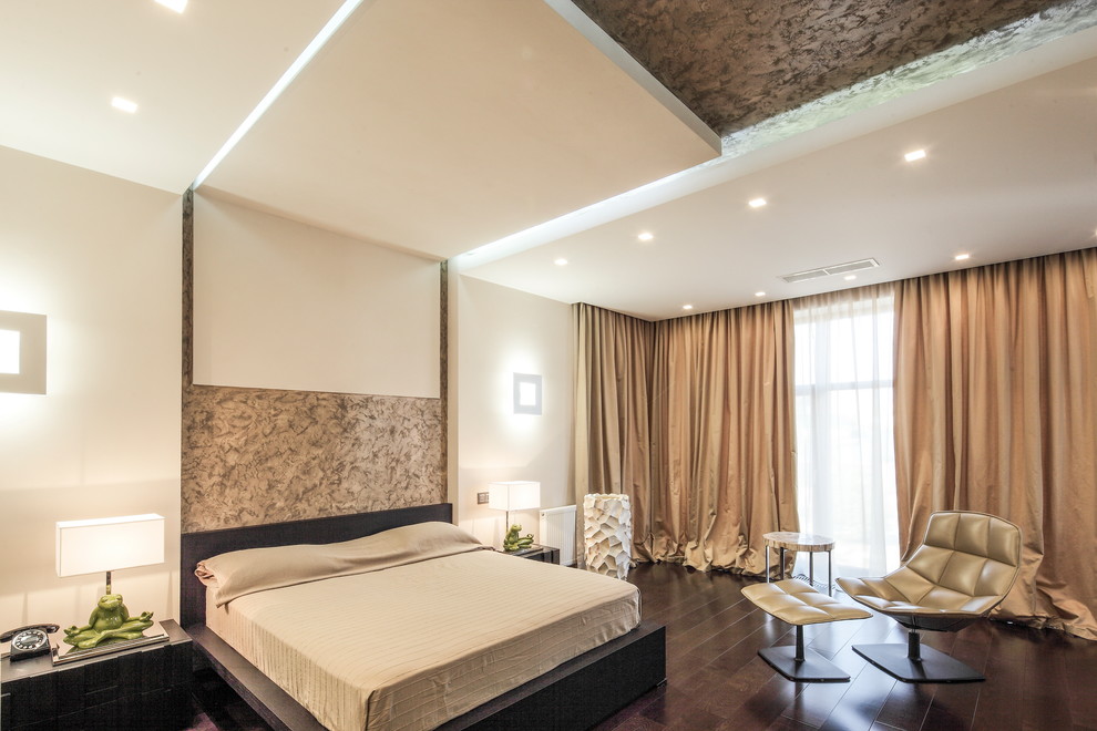 Modelo de dormitorio principal actual grande con paredes beige, suelo de madera en tonos medios y suelo marrón