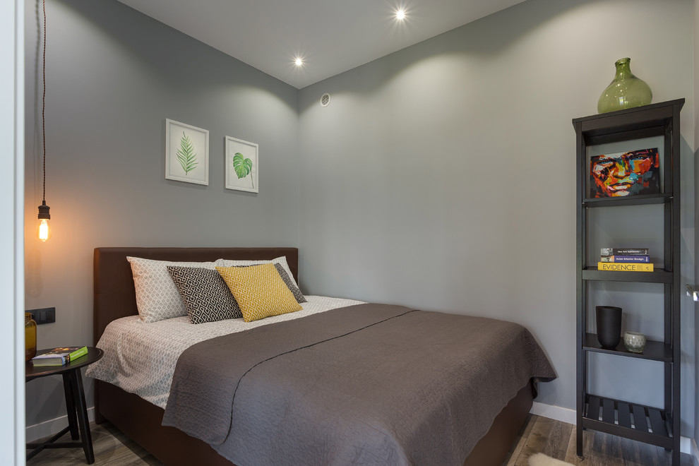 Modelo de dormitorio principal industrial pequeño con paredes grises, suelo laminado y suelo marrón