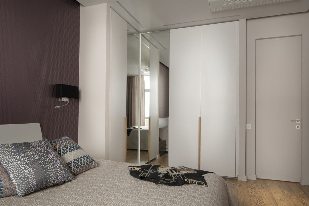 Modelo de dormitorio principal actual grande con paredes púrpuras y suelo de madera en tonos medios